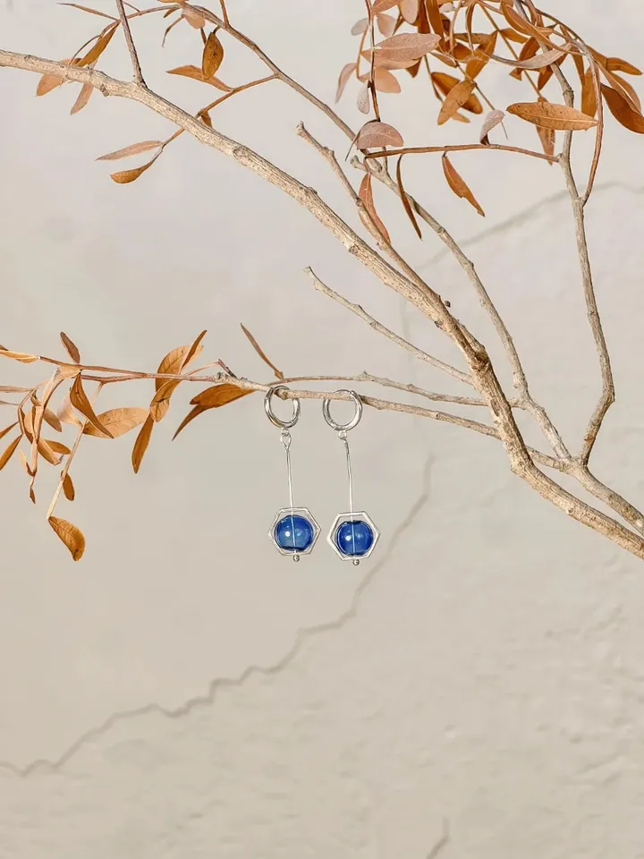 Silver hoop earrings with a deep blue bead, hanging from a dry branch