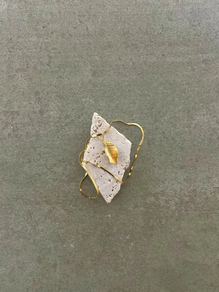 Gold-plated sterling silver necklace with a small golden leaf, laid on a piece of travertine