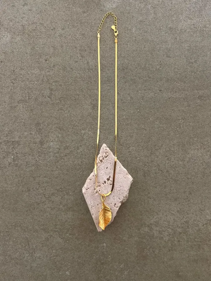 Gold chain necklace with a golden leaf pendant, worn over travertine