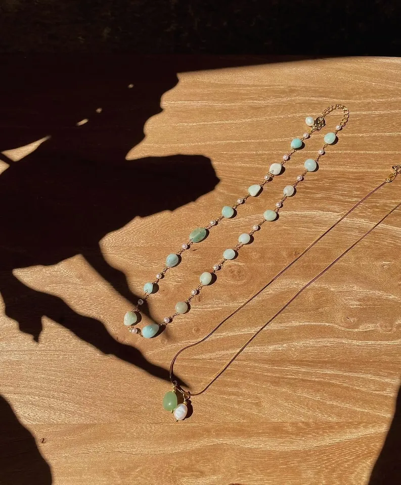 Two fine necklaces with pale green stones on a sunlit wooden table