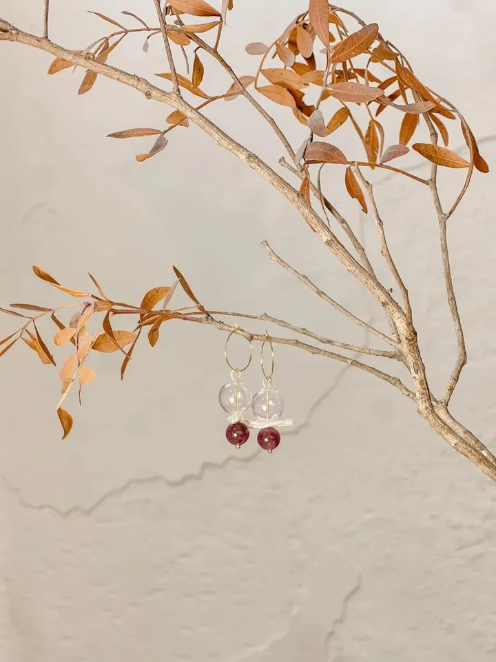 Earrings with clear and deep red beads, hanging from a dry branch