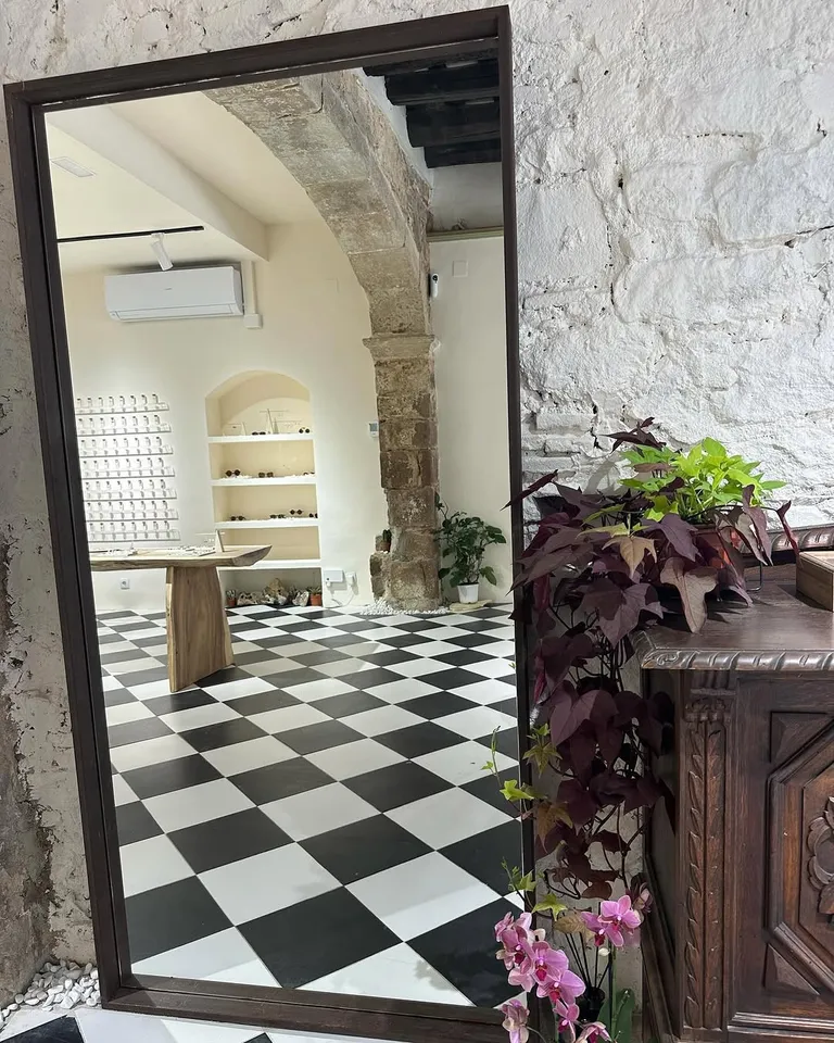 Inside the Tantarantana shop: a tall mirror, a black and white checkerboard floor, stone arches and plants