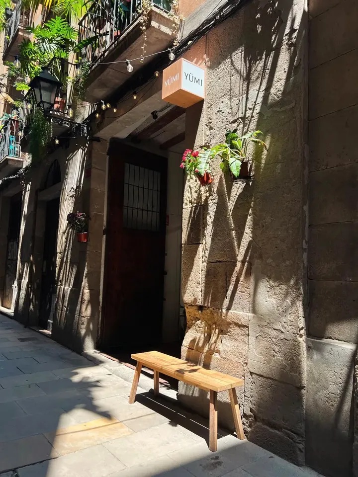 The Yümi shop on Carrer dels Banys Vells, with a wooden bench and plants by the door
