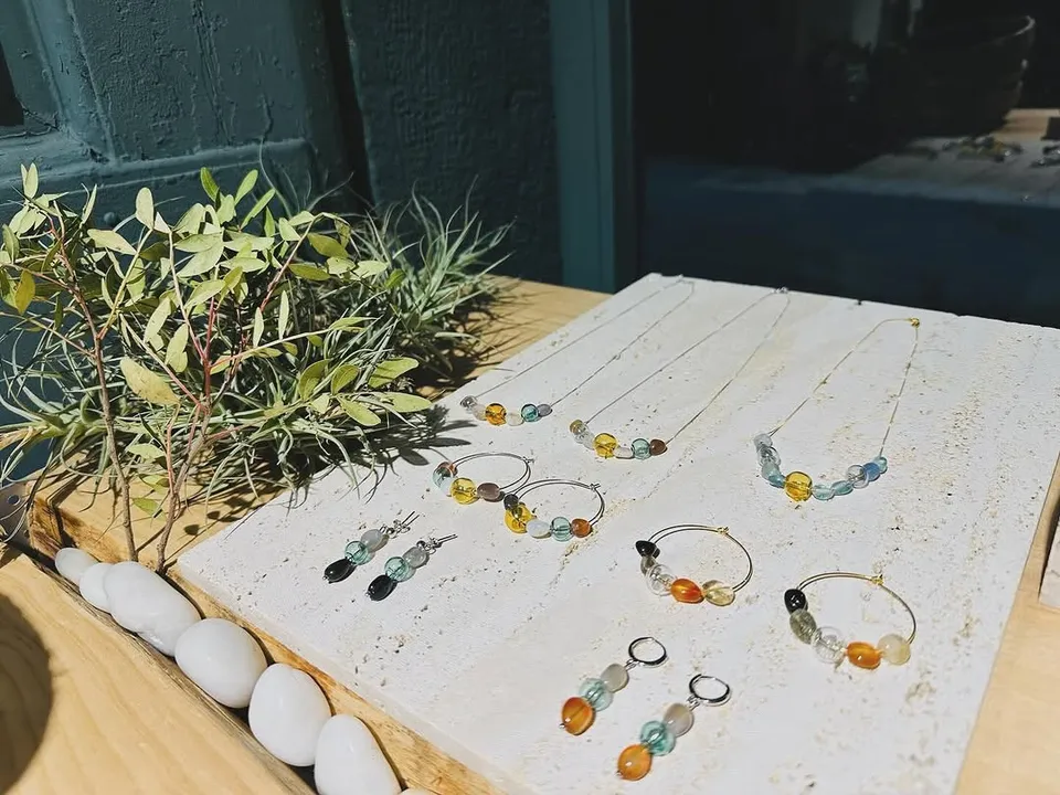 Hoop earrings and fine necklaces with amber, green and blue stones on travertine in the sun